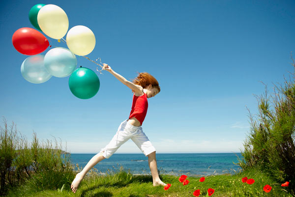 young girl running with colourful balloons against blue sky by Janie Airey photographer