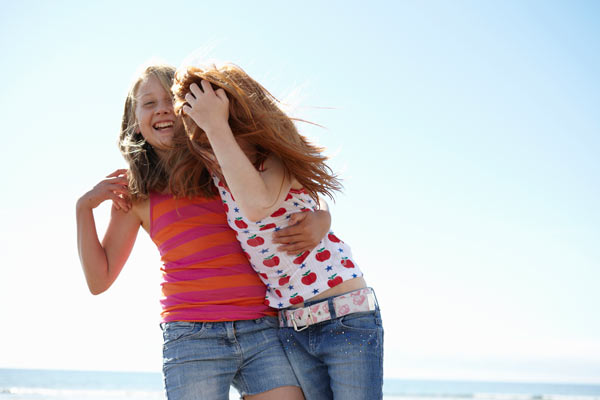 2 girls laughing and hugging on the beach by Janie Airey photographer